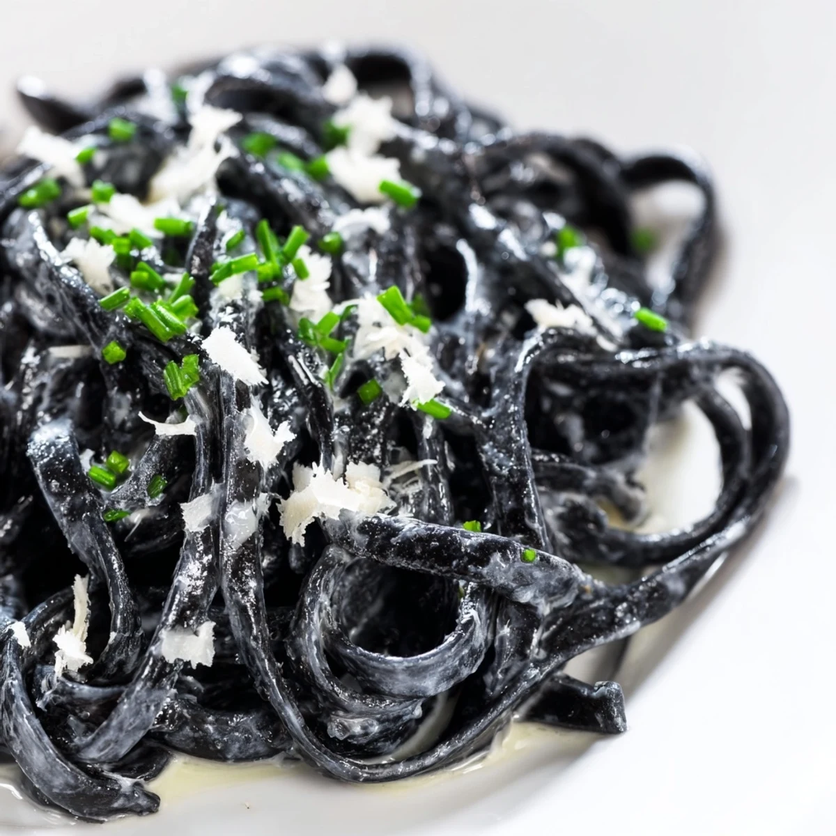 Freshly cooked Squid Ink Pasta strands glisten in a silky cream sauce, topped with grated Parmesan and chopped chives for a dramatic Italian dinner.