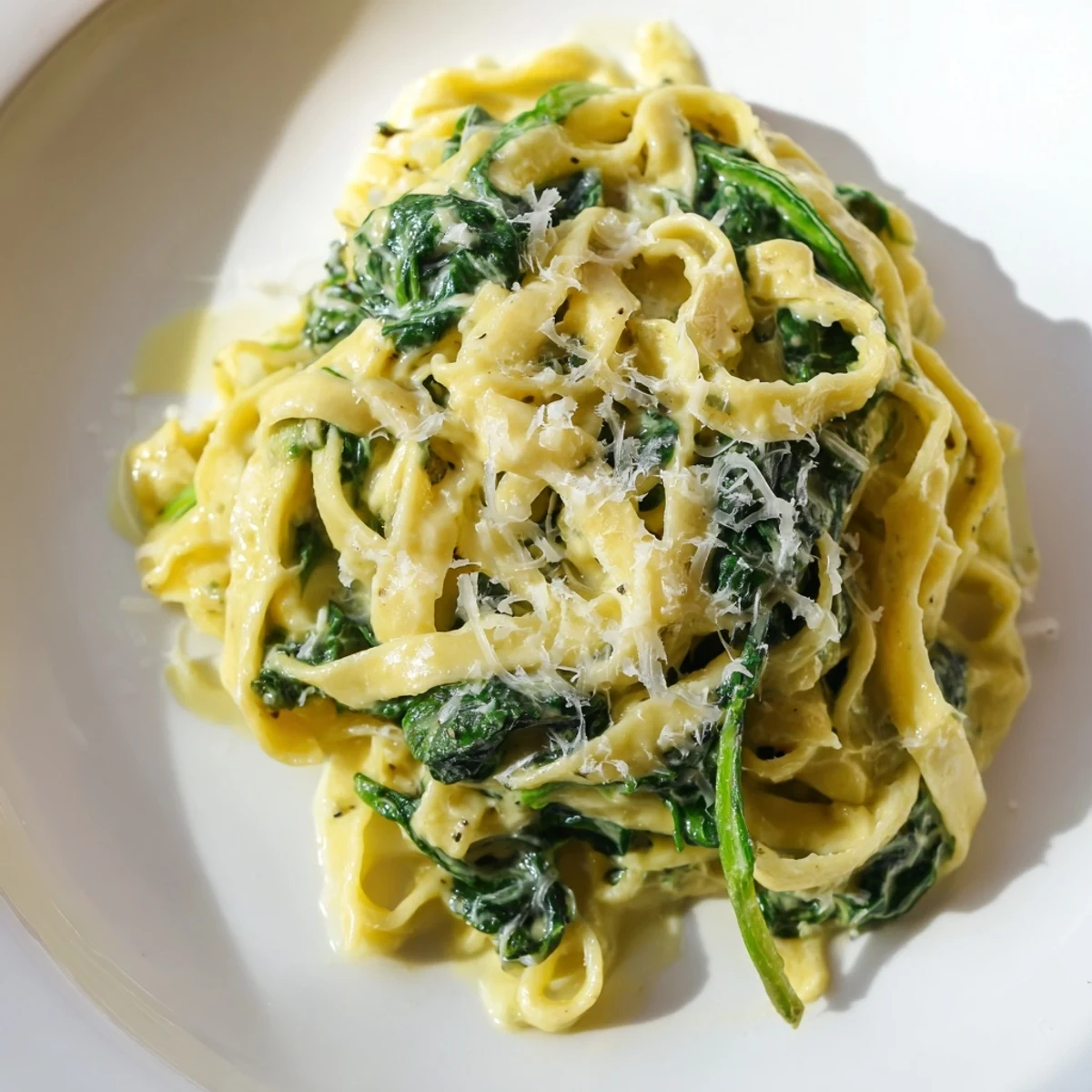 A close-up of Creamy Spinach Garlic Noodles with steaming sauce clinging to silky egg noodles and fresh spinach.  