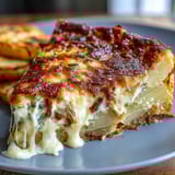 A close-up of baked Cheese and Potato Pie shows tender potato slices and onions enveloped in a rich cream sauce, topped with bubbling, browned cheese.  