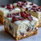 Freshly cut Cranberry Bliss Bars garnished with extra dried cranberries on a rustic wooden serving board.