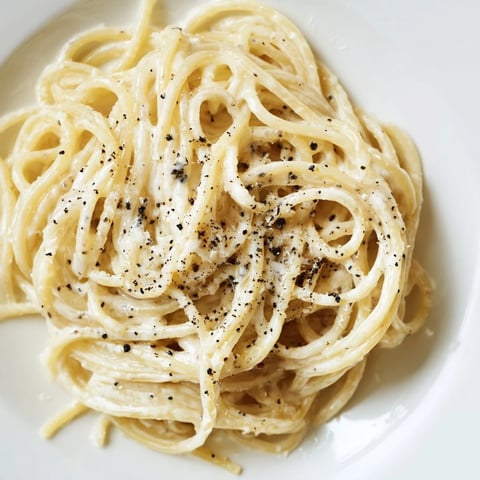 A warm bowl of freshly prepared Spaghetti Cacio e Pepe, twirled with a fork and topped with extra Pecorino Romano cheese and freshly cracked black pepper.