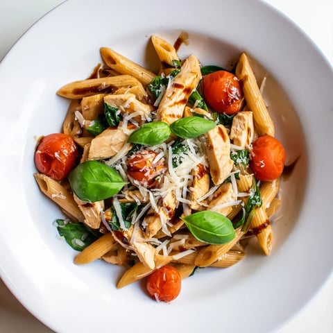 A close-up of Balsamic Glazed Chicken Pasta with glossy penne, tender chicken strips, and bright cherry tomatoes glistening in a rich glaze.  
