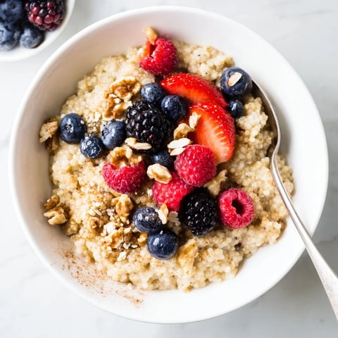 Warm millet porridge topped with vibrant mixed berries, chopped nuts, and a dusting of cinnamon for a cozy breakfast.