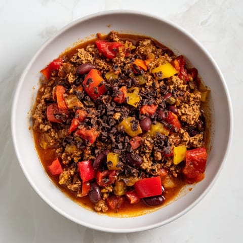 A close-up of hearty One-Pot Cozy Chocolate Chili, glistening and ready to serve with optional garnishes on top.