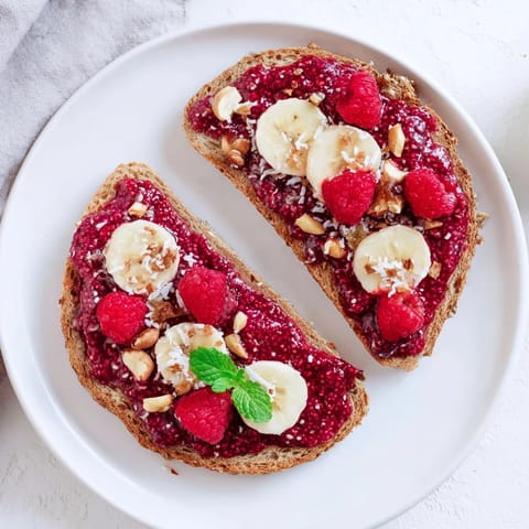 Warm, golden raspberry chia jam toast with fresh, juicy raspberries piled high as a topping.