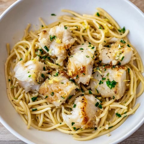 Flaky pan-fried cod or haddock nestles in lemony spaghetti, garnished with parsley and chives for a vibrant, satisfying main dish.