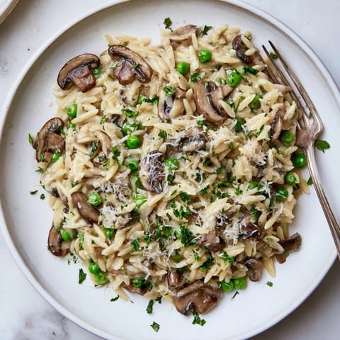 Golden Orzo Mushroom Risotto-Style steaming in a skillet, featuring sautéed cremini mushrooms and tender green peas.