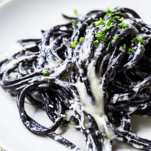Glossy black Squid Ink Pasta is tossed in a rich cream sauce, served with lemon wedges on the side for a bright, luxurious finish.