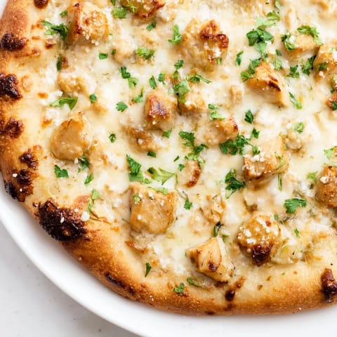 A close-up slice of Chicken Alfredo Pizza reveals bubbly cheese, savory chicken pieces, and a rich Alfredo sauce on a crisp, golden-brown crust.  