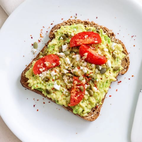 Creamy avocado mash spread on crispy whole grain toast, garnished with red pepper flakes and seeds for a spicy crunch.
