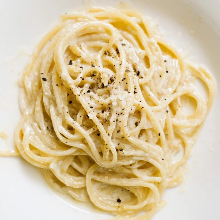 An elegant serving of Spaghetti Cacio e Pepe on a white plate, garnished with a sprinkle of black pepper and a glass of crisp white wine nearby.