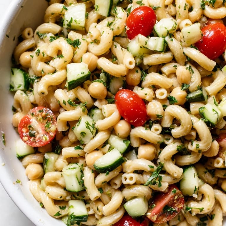 Lemon Herb Chickpea Pasta Salad tossed with crisp cucumbers, tomatoes, and fresh mint on a rustic table.